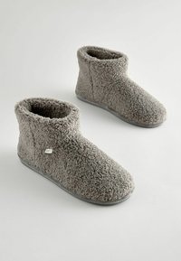 Graue Fleece-Ankelslipper mit weicher Textur, runden Zehen und einer geformten grauen Gummisohle. Mit einem kleinen Logosticker an der Seite.
