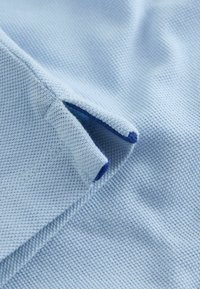 Ljusblått tyg med en texturerad väv och en blå accent vid öppningen. Närbild som framhäver sömnad och färgkontrast.