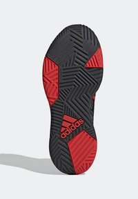 Černá a červená sportovní podrážka obuvi s cikcakovým vzorem a texturovaným povrchem. Jsou viditelné nápisy "Adiwear" a "adidas".