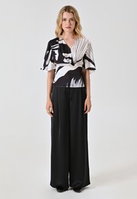 Top avvolgente a maniche corte con motivo in bianco e nero, abbinato a pantaloni neri a vita alta e a gamba larga. Tessuto dal texture morbida.