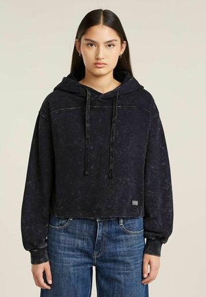 Haut de survêtement noir court avec une finition texturée, capuche avec cordon de serrage et manches longues. Associé à un jean bleu taille haute.