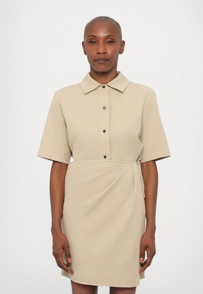 Beige hemdjurk van katoen, met korte mouwen, knopen aan de voorkant en een strik rond de taille voor een wikkel effect. Glad van textuur, eenvoudig ontwerp.