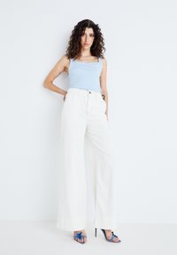 Débardeur côtelé bleu clair associé à un pantalon large blanc. Le mannequin porte des sandales à talons bleu avec des accents en forme de nœud.