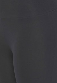 Leggings noires en tissu lisse et extensible. Dotées d'une taille haute et d'un design sans couture, mettant en avant un look lisse et ajusté.