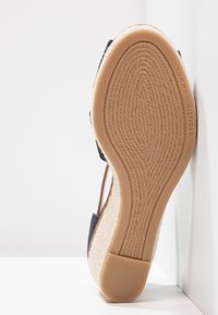 Semelle de sandale avec fond en caoutchouc beige texturé et marquage "Tommy Hilfiger", talon compensé avec matériau en fibres naturelles tissées.