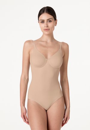 Donna con capelli scuri in una body modellante color nude senza cuciture, su sfondo bianco uniforme.
