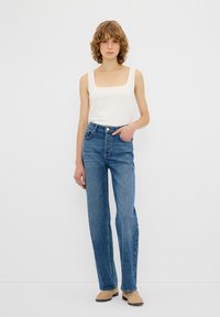 Jeans in denim blu con design a gamba dritta, vita alta e stile a cinque tasche. Abbinati a un top bianco semplice e scarpe beige.