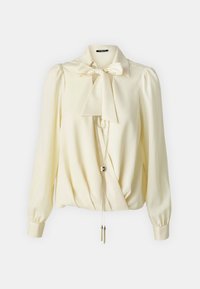 Blusa crema con colletto a fiocco, maniche lunghe e puff, design incrociato e dettagli metallici, caratterizzata da una catena con estremità pendenti.