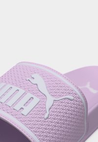 Κοντινή λήψη ενός σανδάλου Puma slide σε λιλά απόχρωση, με υφασμένη λουριά που φέρει το λευκό λογότυπο και τη σήμανση Puma.