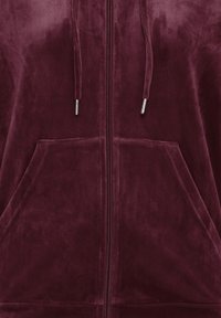 Gros plan d'un sweat à capuche en tissu doux de couleur grenat avec fermeture éclair à l'avant, cordons et coutures visibles de la poche kangourou.