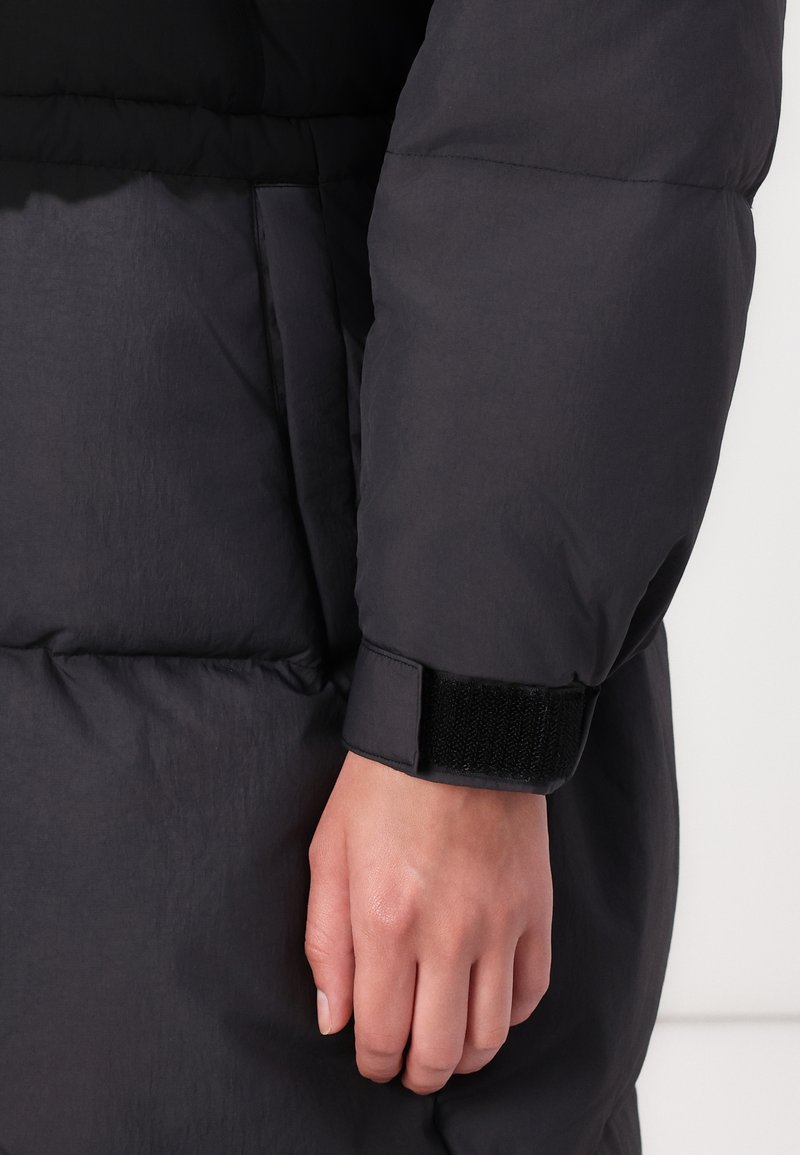 Schwarzer Pufferschulterärmel mit strukturierter Oberfläche, ausgestattet mit einem anliegenden Bündchen, das durch einen schwarzen Klettverschluss gesichert ist, und einem leicht gepolsterten Design.