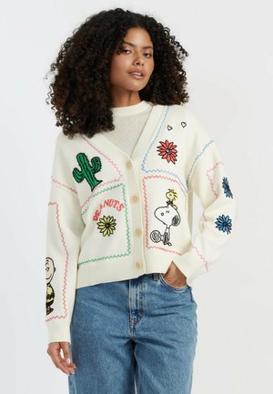 Cream cardigan with multi-colored embroidered patches featuring plants and characters. Button closure, relaxed fit, ribbed cuffs and hem.