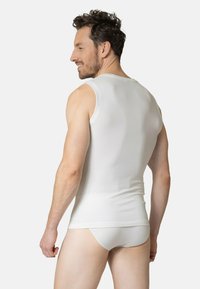 White sleeveless tank top with a textured finish, fitted design, and round neckline, paired with white briefs, viewed from the back.