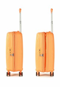 Valise rigide orange avec texture linéaire, poignée rétractable, fermeture éclair et quatre roues pour la mobilité. Équipée d'une serrure à combinaison.
