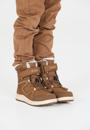 Bottes imperméables marron avec doublure en fourrure, dotées de sangles ajustables, d'un dessus texturé et de semelles en caoutchouc. Décorées de motifs en zigzag.