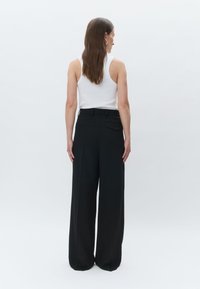 Črne široke hlače z visokim pasom, s enim hrbtnim žepom in subtilno teksturo. Model nosi belo majico brez rokavov.