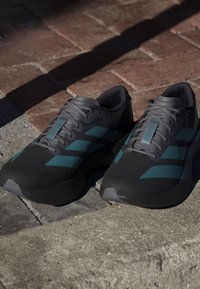 Czarne buty sportowe z akcentami w odcieniu teal, o smukłej konstrukcji, teksturowanym materiale cholewki i aerodynamicznym kształcie dla lepszej wydajności.