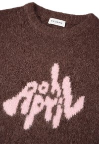 Rjav pleten pulover z mehko teksturo, na katerem se po sprednji strani v igrivem tisku ponaša rožnati stilizirani logotip "OH APRIL".
