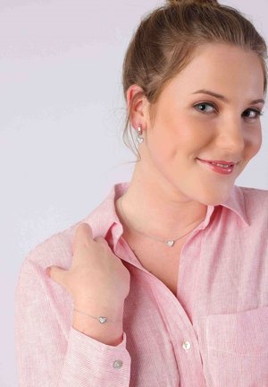 Zilveren hartvormige sieraden omvatten oorbellen, een ketting en een armband. De oorbellen hebben een hoepelontwerp en een glanzende afwerking.