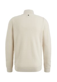 Lichtbeige pullover met een textuurgebreid patroon, hoge kraag en geribde boorden en zoom. Bevat een klein embleem op de achterkant.
