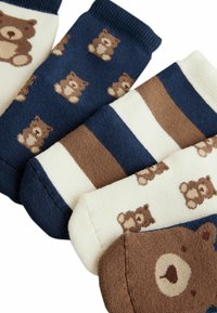 Quattro paia di calzini con design di orsi. I colori includono blu navy, crema e marrone con motivi di orsi e righe. Texture morbida osservata.