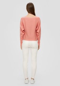 Rosa gerippter Pullover mit weitem Ausschnitt, kombiniert mit weißen Skinny Jeans und weißen Sneakers, von hinten betrachtet.