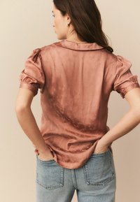 Rosa satinbluse med puffede ærmer og krave, med et subtilt blomstermønster, parret med lyseblå denim jeans.
