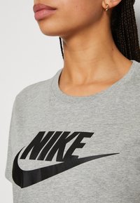 Pilkas medvilninis marškinėliai su dideliu juodu Nike logotipu ant krūtinės, apvaliu iškirpimu ir trumpomis rankovėmis.