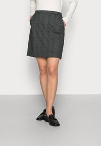 Falda gris texturizada, hasta la rodilla, con bolsillos laterales, combinada con mocasines negros. Diseño minimalista, corte a medida y dobladillo recto.