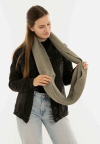 Scaldino infinito grigio chiaro lavorato a maglia, texture morbida, con un motivo a coste e foderatura liscia, appoggiato attorno al collo di un modello.