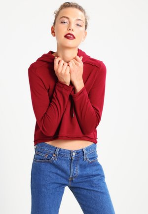 Burgundská skrátená mikina s dlhými rukávmi a kapucňou na sťahovanie. V kombinácii s modrými denimovými džínami s vysokým pásom. Minimalistický dizajn.
