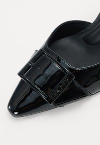 Sorte patentlæder spidse sko med en bred rem og firkantet spænde samt præget branding, glat tekstur og læderinteriør.