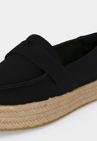 Chaussure noire à enfiler avec semelle plateforme beige tressée et large bride sur le dessus pour un usage décontracté.