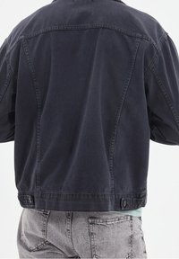 Tmavě námořnická džínová bunda s volným střihem, viditelnými švy a zapínáním na knoflíky na lemu. Hladká textura s mírně vybledlým vzhledem.