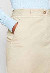 Beige kjol med en slät yta, utrustad med sidofickor och knäppning med knapp. Matchas med en ljusblå, kabelstickad tröja.