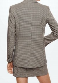 Ruudullinen blazer, jossa on muotoiltu istuvuus mustavalkoisena. Takissa on leikattu kaulus, kaksinappinen sulkeminen sekä yksittäinen halkio takana.