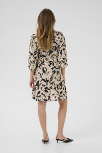 Blommigt mönstrad klänning i beige, svart och rosa toner; har 3/4-ärmar, en avslappnad passform och slutar ovanför knäet. Bärs med svarta klackar.