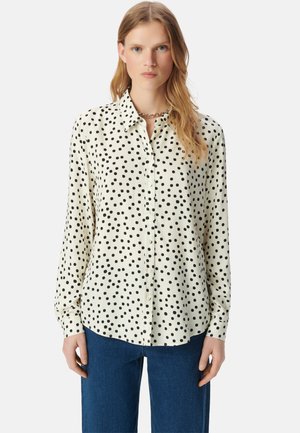 Camicia bianca con pois neri, maniche lunghe e colletto. Abbinata a pantaloni in denim blu. Tessuto liscio e vestibilità comoda.