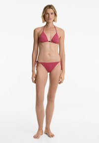 Bikini v rdečih in roza vzorcih, ki vključuje triangularni zgornji del s povezavami za vrat in nastavljivimi spodnjimi deli s kravato ob straneh. Gladek material, minimalna oprema.
