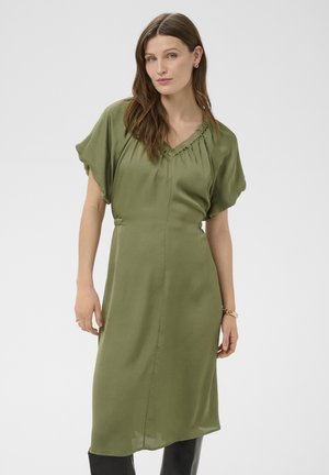 Femme portant une robe midi vert olive avec des manches courtes froncées, posant devant un fond blanc uni.