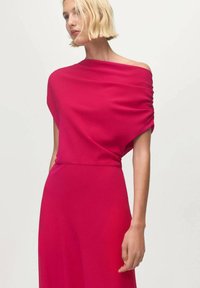 Vestido fucsia con hombros descubiertos y tela drapeada, con detalles fruncidos en los hombros y una silueta fluida. Textura suave y ligera.
