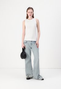 Hvit ribbestrikket tanktop kombinert med lyseblå vide jeans, holder en liten svart håndveske. Enkelt design med en avslappet passform og teksturer.