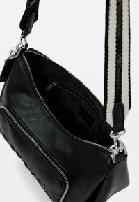 Schwarze Lederhandtasche mit einem Reißverschluss, mit einer strukturierten Außenseite, silbernen Beschlägen und einem gestreiften, verstellbaren Tragegurt. Das Innere ist schlicht schwarz.