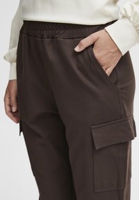 Bruine cargobroek met een elastische tailleband en zijzakken, met een zachte textuur en een patchzak op de dij.