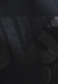 Tela atlética negra con un diseño texturizado y letras grandes en relieve. La superficie combina detalles lisos y con textura.