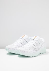 Bílé sportovní boty s vrškem z prodyšné síťoviny, světlými mátovými akcenty a texturovanou podešví. Obsahují značkovou nášivku na jazyku a zesílenou oblast pro šněrování.