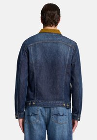 Giacca di denim con una finitura blu scuro, caratterizzata da un colletto color senape, polsini con bottoni e una silhouette classica con dettagli sul retro.