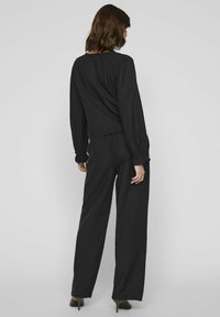 Top negro de manga larga con hombros ligeramente abombados, combinado con pantalones anchos negros. Tela suave, corte casual y sin patrones visibles.