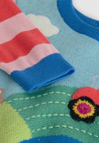 Knitted sweater featuring a blue body, red and pink striped sleeves, and embroidered tractor and flower details on a green landscape design.