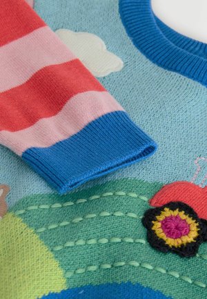 Sweter dzianinowy z niebieskim korpusem, czerwono-różowymi rękawami w paski oraz haftowanymi detalami przedstawiającymi ciągnik i kwiaty na zielonym tle.